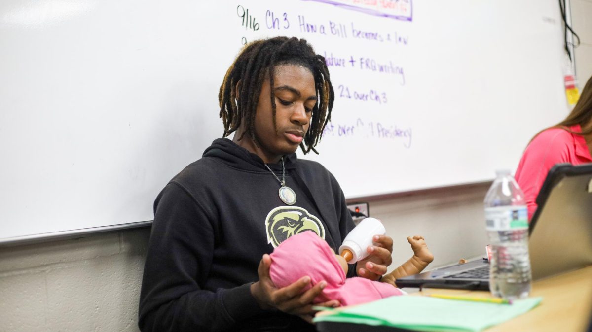 Holding his fake baby's head, sophomore Jakari Haskin feeds the baby before logging the information.