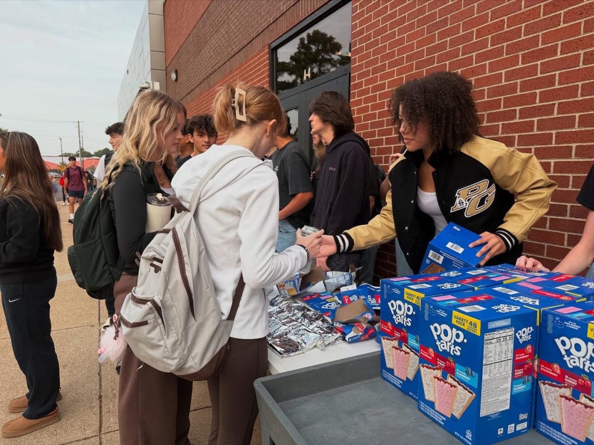 Setting a Poptart box down, senior Alexia Gipson hands a Poptart to sophomore Olivia Wyatt (left) and senior Charlotte Clark (right).