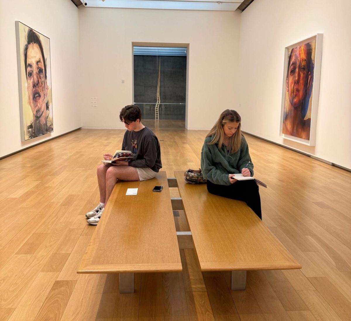 Sketching in their art journals, sophomore Caden McCullough [left] and junior Sidney Story, [right] study the artwork lining the walls. 